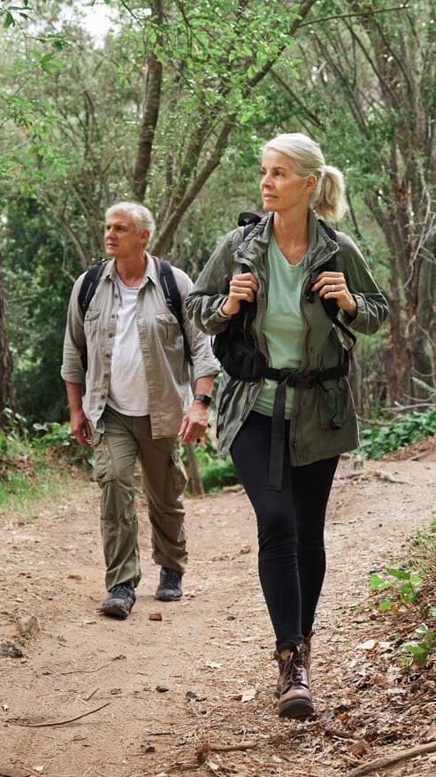 Active older couple hiking together on a forest trail, enjoying the outdoors after pain treatment at Pain Doctors Medical