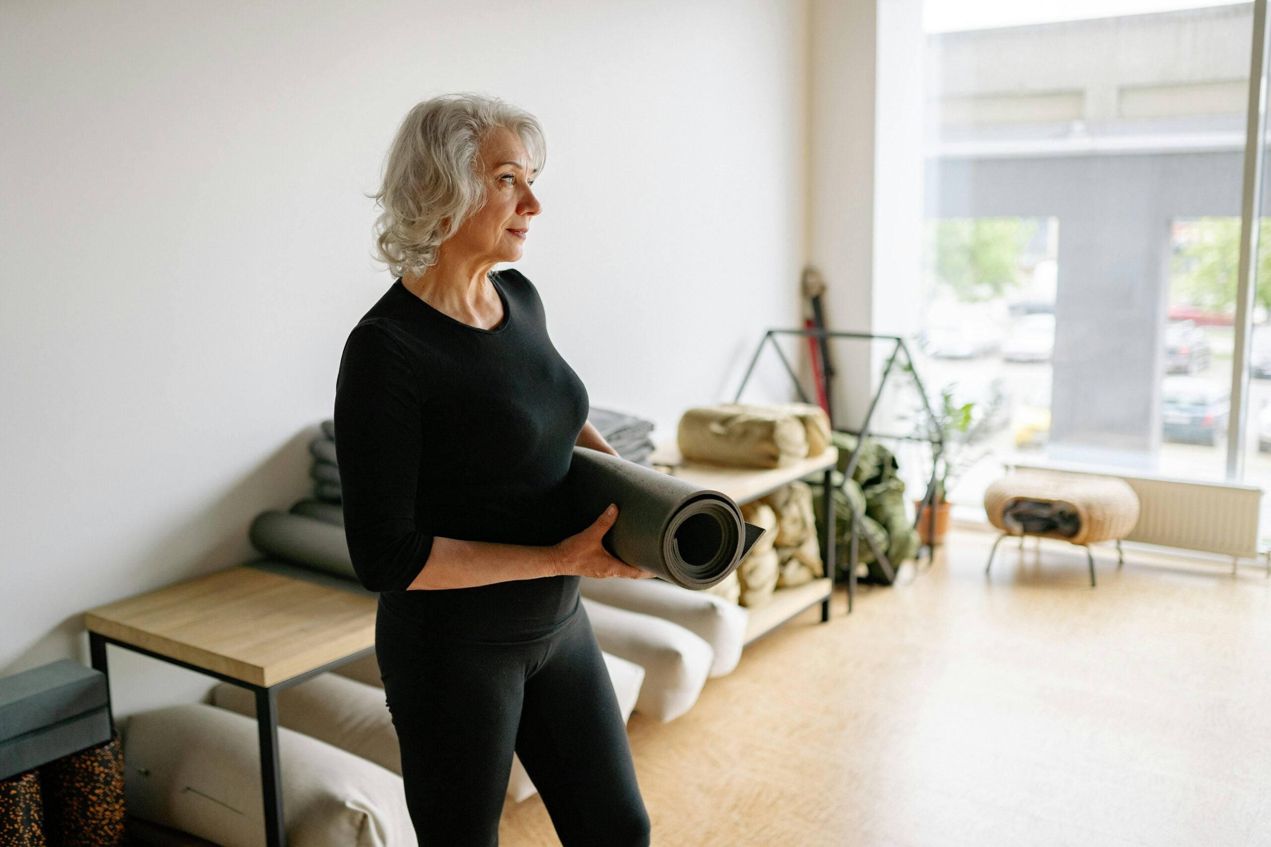 Active older woman in fitness wear holding a yoga mat, ready to return to movement after treatment