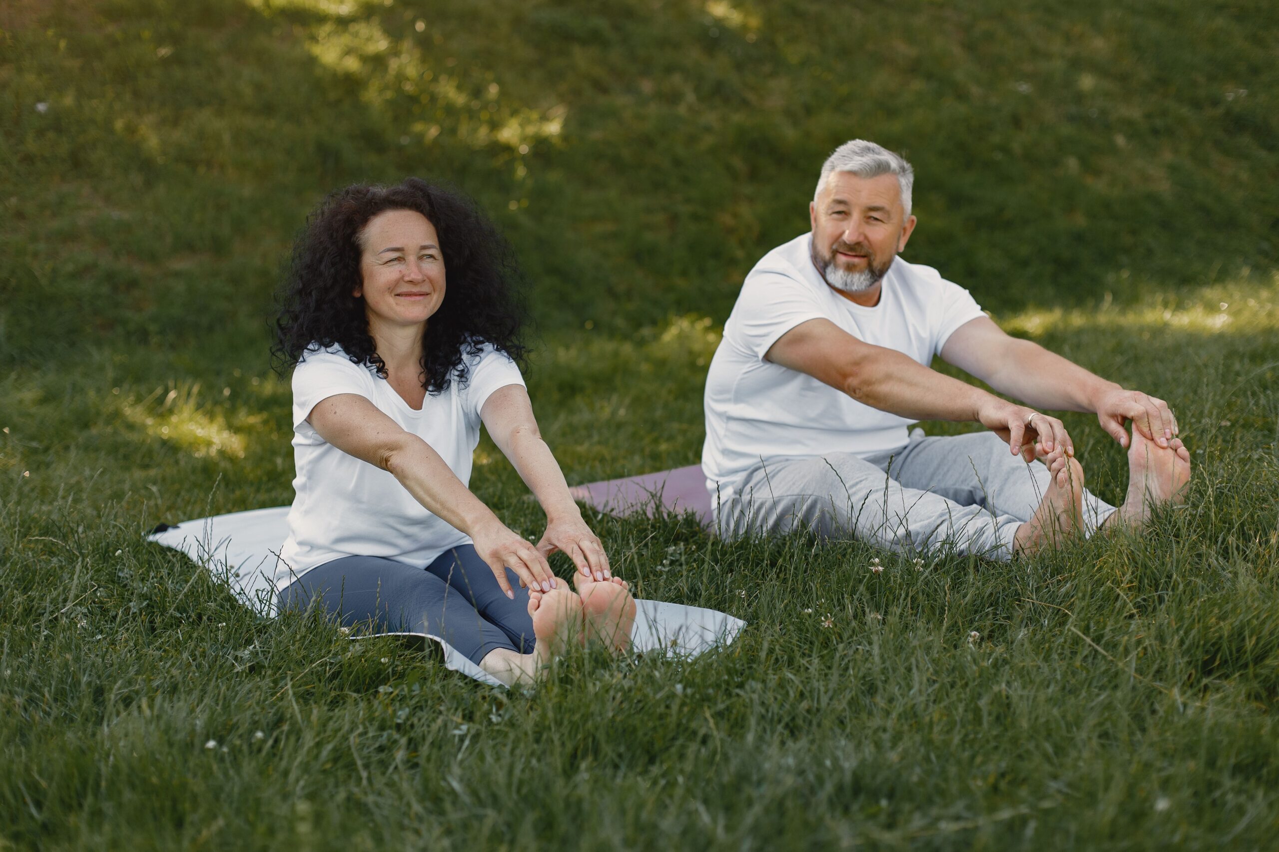 Active mature couple stretching outdoors on the grass, staying mobile after regenerative medicine care at Pain Doctors Medical Clifton