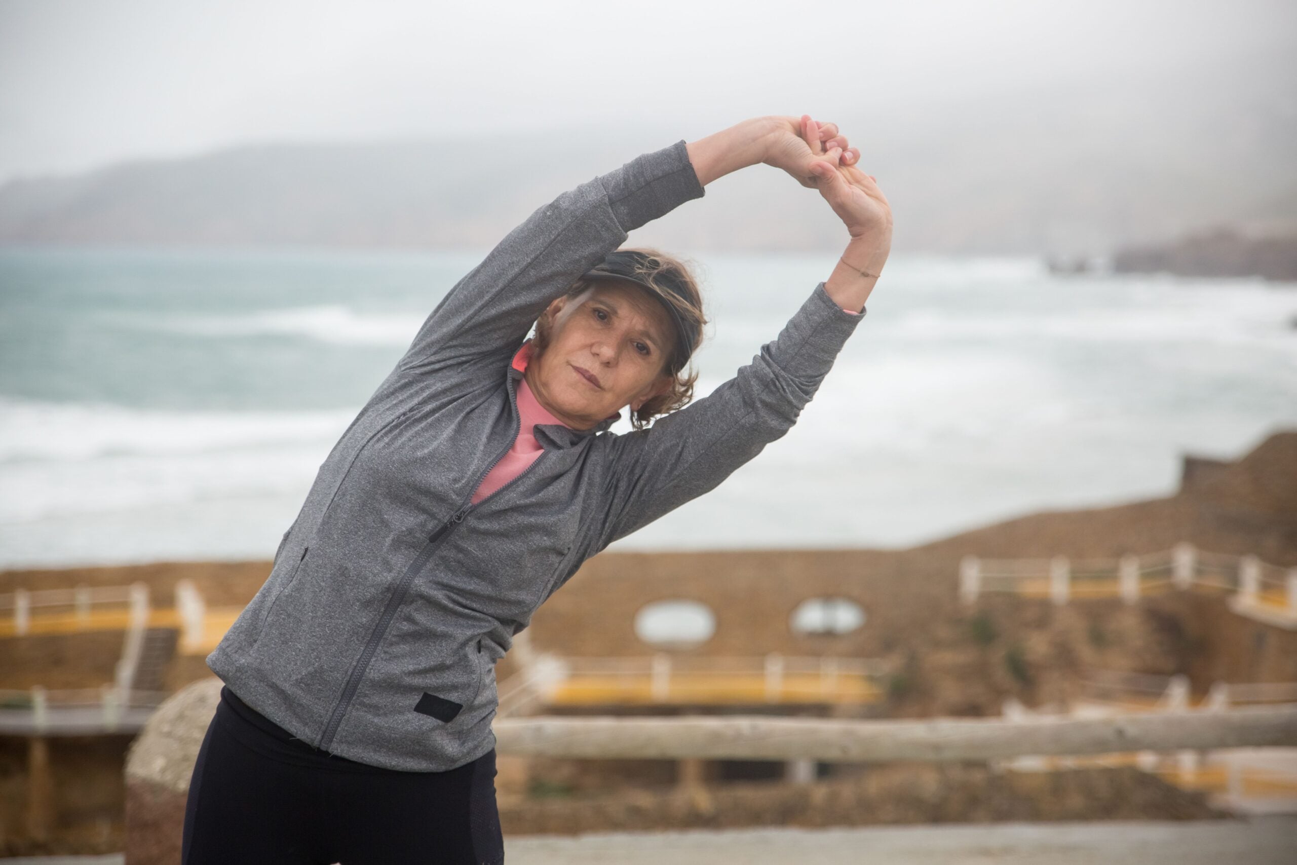 Active older woman stretching outdoors by the coast, staying mobile after regenerative medicine care at Pain Doctors Medical Newark